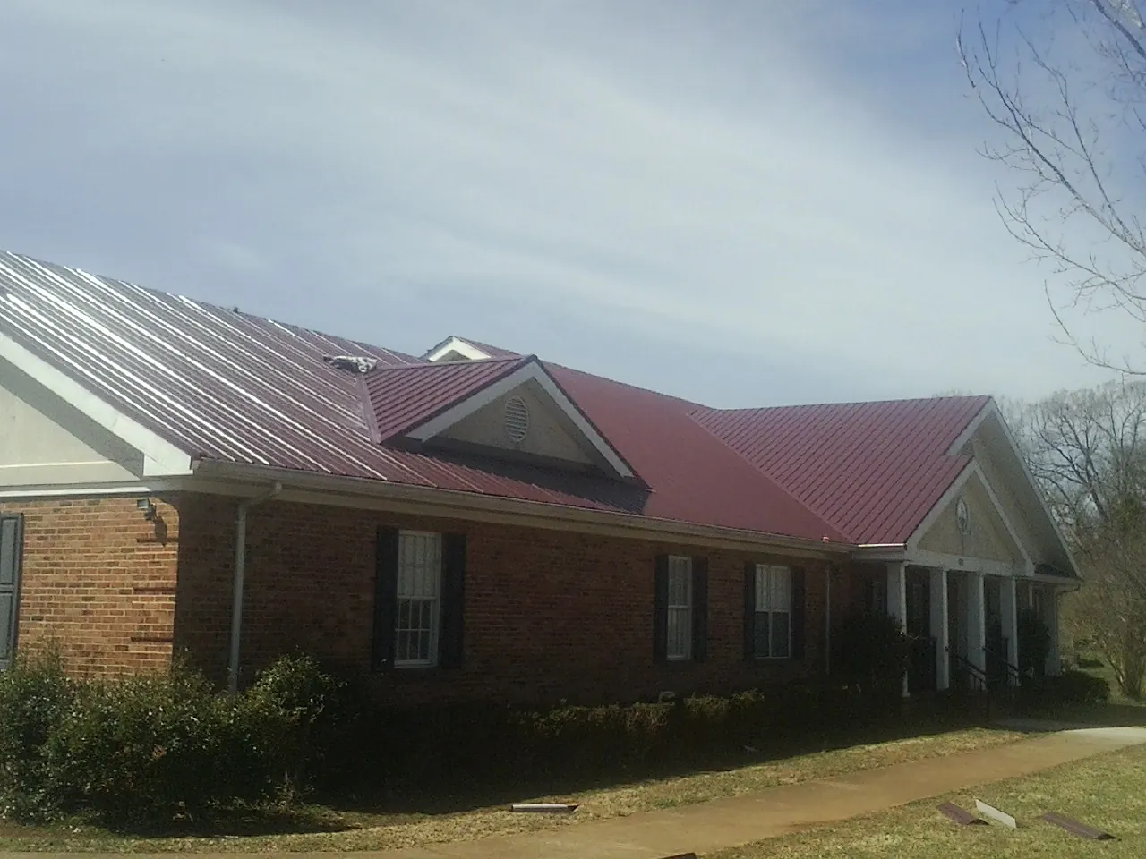 Red metal roof with gabled entries on a long brick building, from a Hail Damage Roof Repair job in Amlin