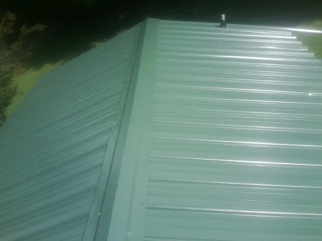 New green metal panels meeting at the ridge of a roof — Flat Roof Repair work by our crew in Amlin
