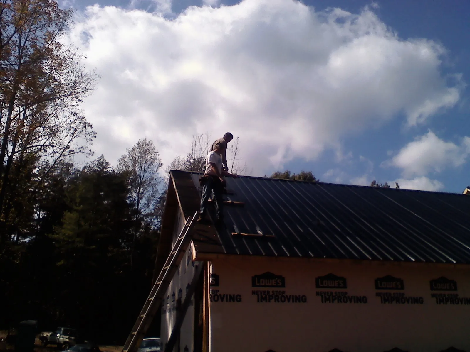 Roofer fastening dark metal panels high against a cloudy sky, from a Roof Inspection job in Amlin