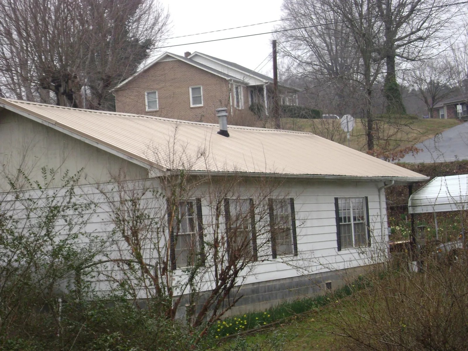 Tan metal roof on a white sided house set into a hillside — Commercial Roofing by Roofing Brothers in Amlin