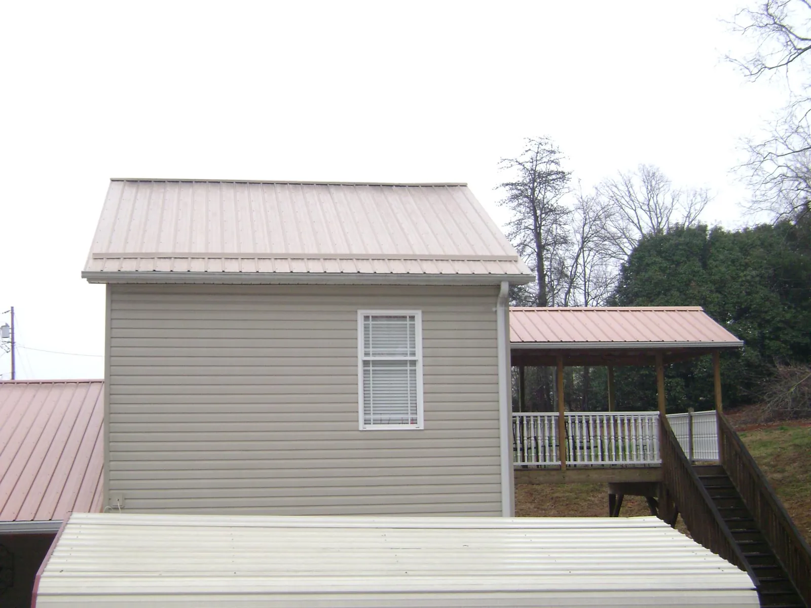 Tan metal roofs on a two story addition and attached porch, from a Roof Replacement job in Amlin
